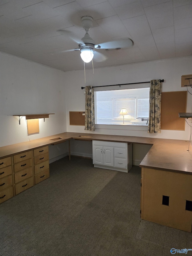 unfurnished office with carpet flooring, a ceiling fan, and built in desk