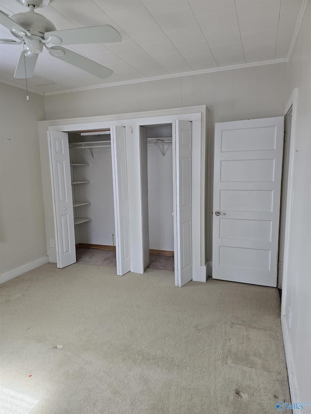 unfurnished bedroom featuring multiple closets, light carpet, a ceiling fan, crown molding, and baseboards