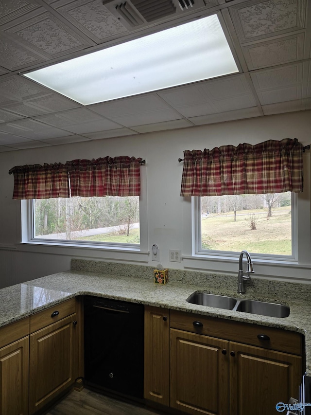 kitchen featuring a sink, light stone counters, black dishwasher, and brown cabinetry