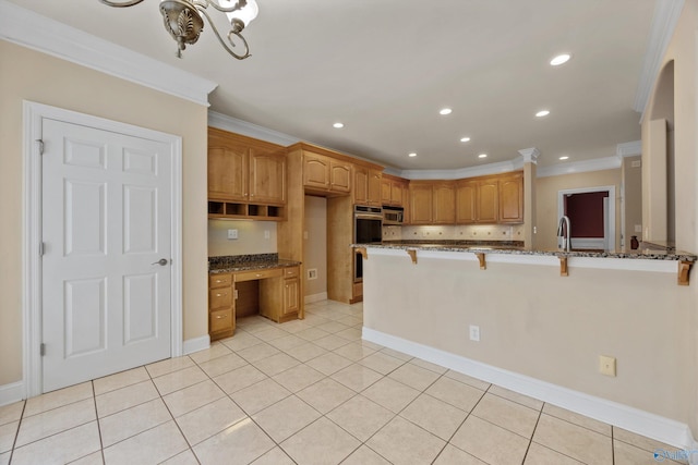 kitchen featuring crown molding, dark stone counters, a kitchen breakfast bar, and built in desk