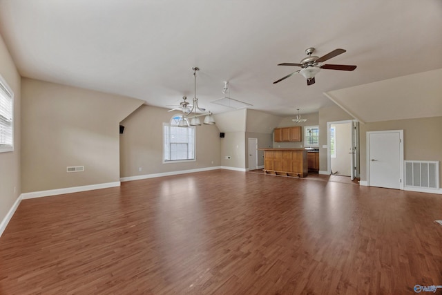 unfurnished living room featuring plenty of natural light, ceiling fan with notable chandelier, wood finished floors, and visible vents