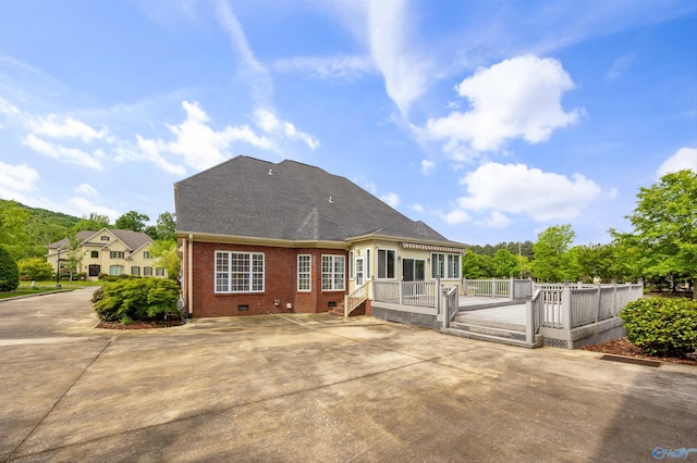 back of property with crawl space, roof with shingles, a deck, brick siding, and fence