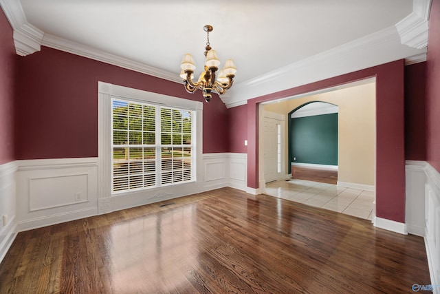 unfurnished dining area with crown molding, arched walkways, wood finished floors, a wainscoted wall, and a notable chandelier