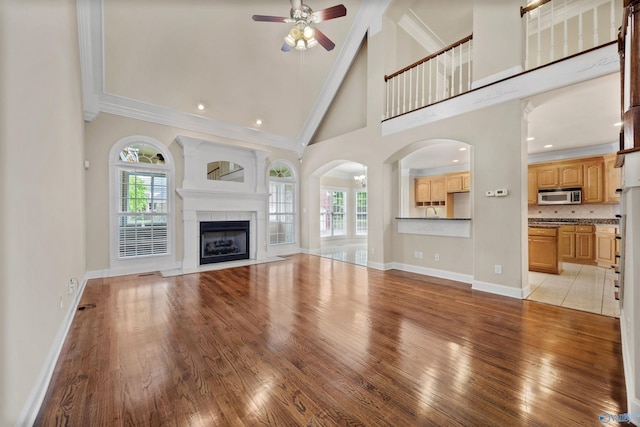 unfurnished living room with light wood-style floors, high vaulted ceiling, a ceiling fan, baseboards, and ornamental molding