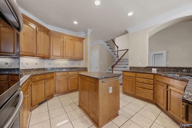 kitchen with a center island, arched walkways, dark stone countertops, backsplash, and light tile patterned floors