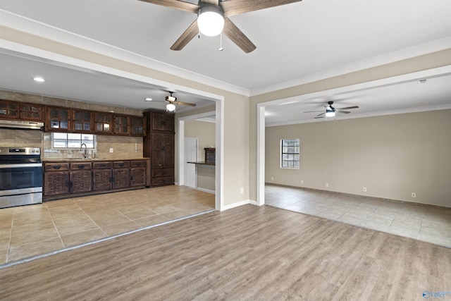 unfurnished living room with light wood-style flooring, baseboards, ornamental molding, a ceiling fan, and a sink