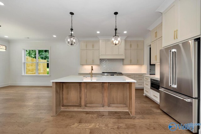 kitchen featuring high end fridge, a center island with sink, sink, backsplash, and light hardwood / wood-style floors