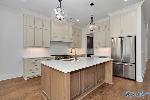 kitchen featuring stainless steel built in refrigerator, backsplash, a kitchen island with sink, light hardwood / wood-style floors, and light stone countertops