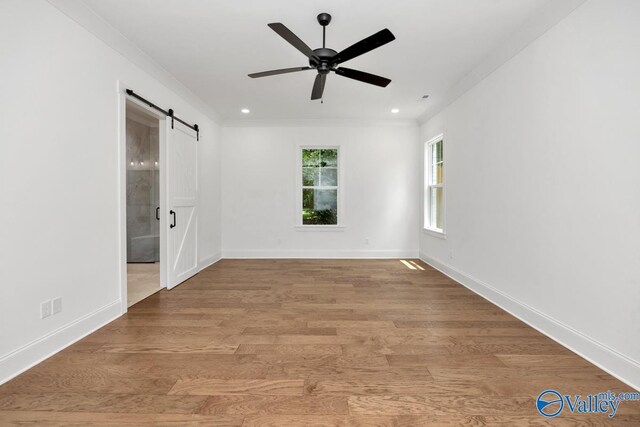 empty room featuring light hardwood / wood-style floors, crown molding, a barn door, and ceiling fan