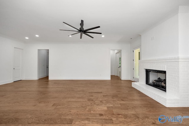 unfurnished living room with ceiling fan, ornamental molding, hardwood / wood-style flooring, and a brick fireplace