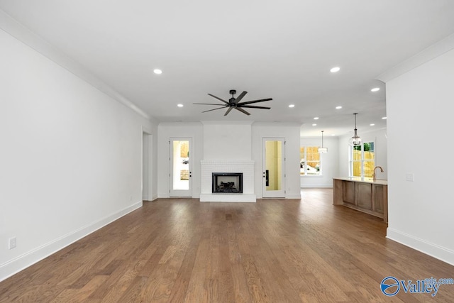 unfurnished living room with crown molding, wood-type flooring, a brick fireplace, and ceiling fan