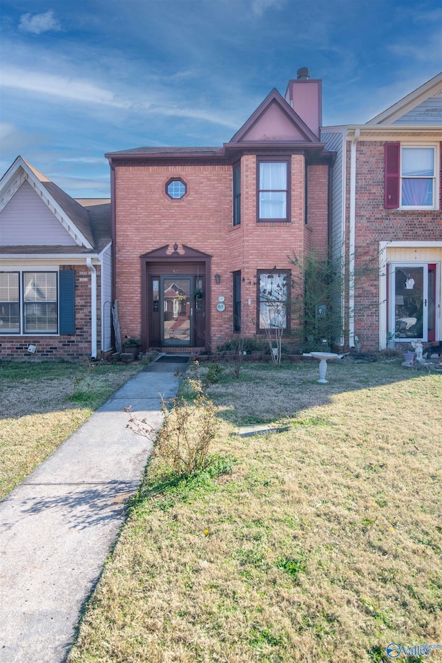 view of front of house with a chimney, brick siding, and a front yard