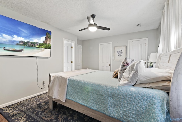 bedroom featuring a ceiling fan, a textured ceiling, multiple closets, baseboards, and visible vents