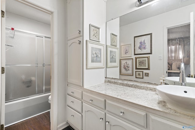 full bathroom with toilet, vanity, bath / shower combo with glass door, and wood finished floors