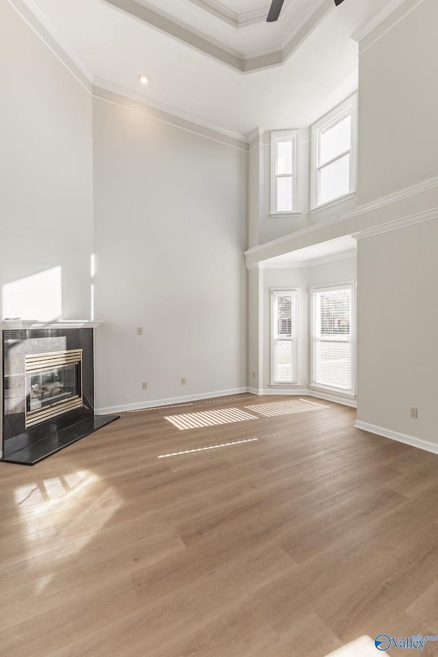 unfurnished living room with ceiling fan, crown molding, a tile fireplace, and light hardwood / wood-style flooring