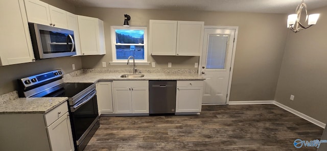 kitchen with appliances with stainless steel finishes, light stone counters, sink, white cabinets, and hanging light fixtures