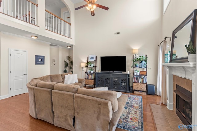 living room featuring a tiled fireplace, wood finished floors, visible vents, and a ceiling fan