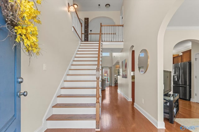 foyer with ornamental molding, a towering ceiling, baseboards, and wood finished floors