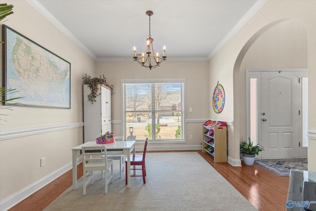 dining area featuring ornamental molding, arched walkways, wood finished floors, and a chandelier