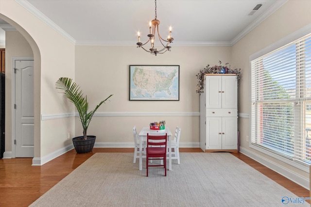 dining area with arched walkways, wood finished floors, visible vents, baseboards, and crown molding