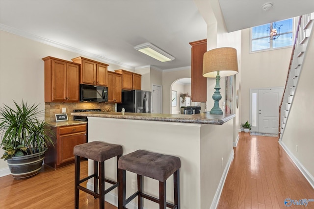 kitchen featuring stainless steel fridge with ice dispenser, a breakfast bar, brown cabinets, black microwave, and backsplash