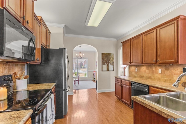 kitchen featuring arched walkways, light wood-style floors, ornamental molding, a sink, and black appliances