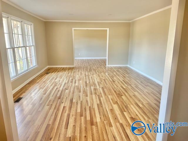 unfurnished room featuring light wood-style flooring, visible vents, baseboards, and ornamental molding