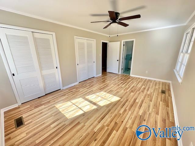 unfurnished bedroom featuring light wood-style flooring, visible vents, baseboards, multiple closets, and ornamental molding