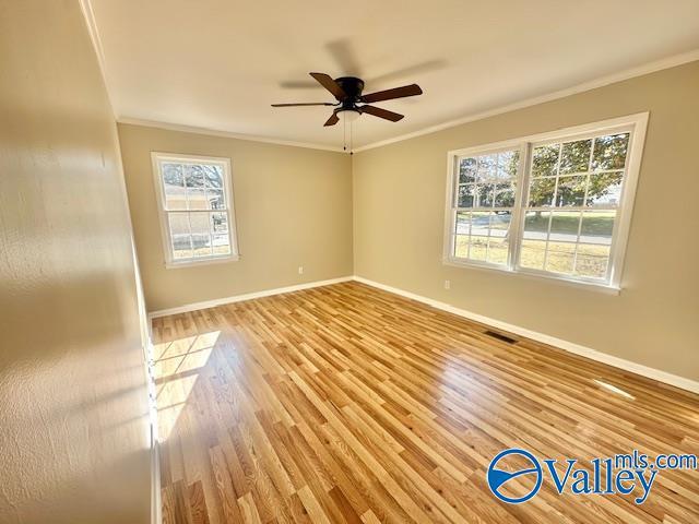 spare room featuring ornamental molding, light wood-type flooring, visible vents, and baseboards