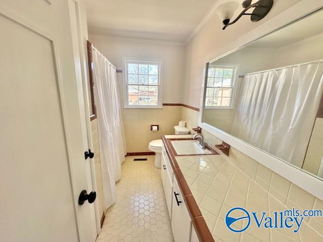 full bath with tile walls, toilet, wainscoting, vanity, and tile patterned flooring