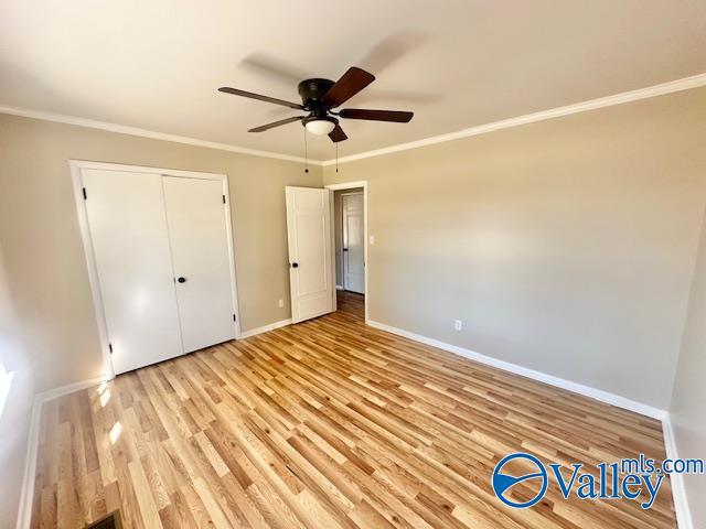 unfurnished bedroom featuring baseboards, a ceiling fan, ornamental molding, light wood-style floors, and a closet