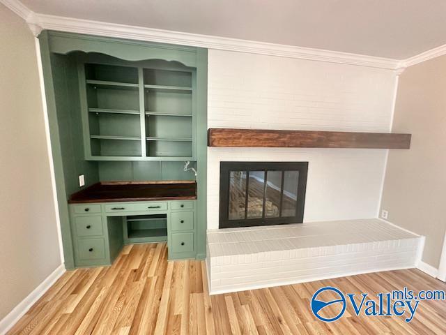 interior space featuring baseboards, a glass covered fireplace, light wood-style flooring, and crown molding