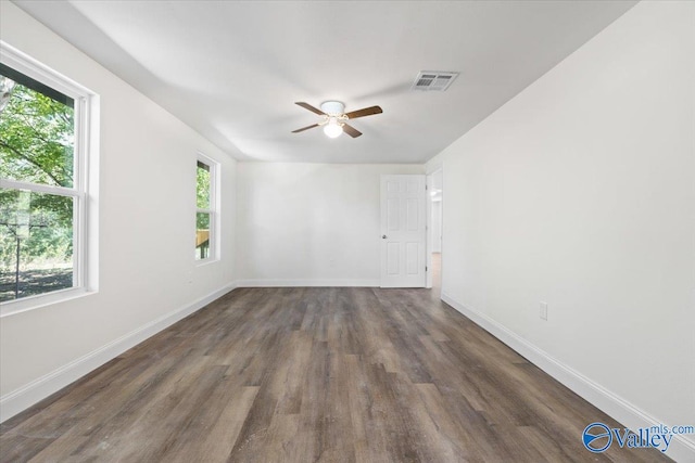 empty room featuring a healthy amount of sunlight, ceiling fan, and dark hardwood / wood-style flooring