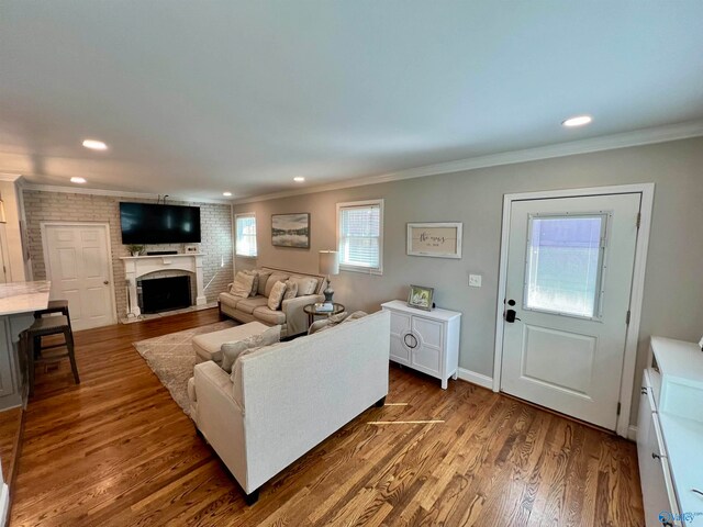 living room with a fireplace, crown molding, dark wood-type flooring, and brick wall