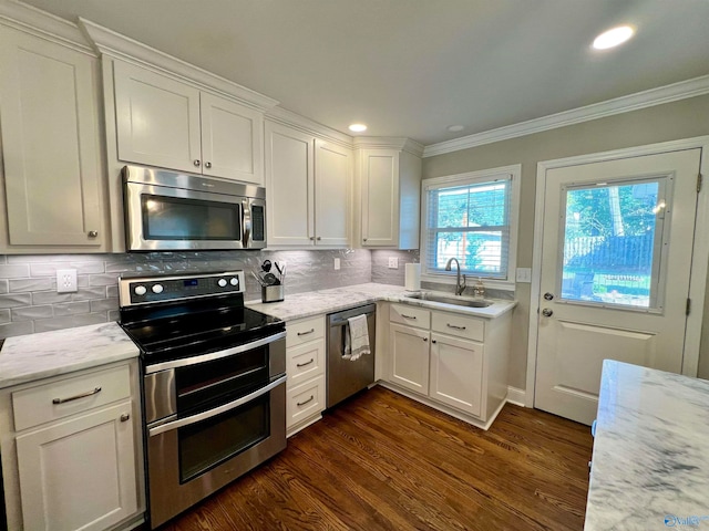 kitchen with light stone counters, dark hardwood / wood-style flooring, appliances with stainless steel finishes, white cabinets, and ornamental molding