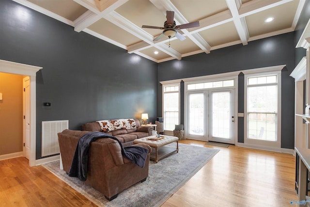 living room with ceiling fan, beamed ceiling, coffered ceiling, a high ceiling, and light hardwood / wood-style floors