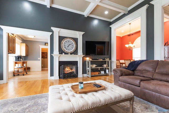 living room featuring light hardwood / wood-style floors, a fireplace, beamed ceiling, crown molding, and an inviting chandelier