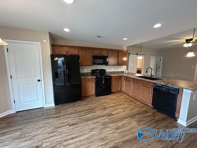 134 Winstead Cir, Owens Cross Roads, AL 35763 - kitchen with a sink, black appliances, a peninsula, brown cabinetry, and wood finished floors