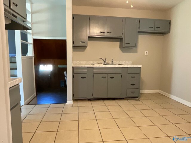 kitchen with light countertops, a sink, gray cabinetry, and light tile patterned floors