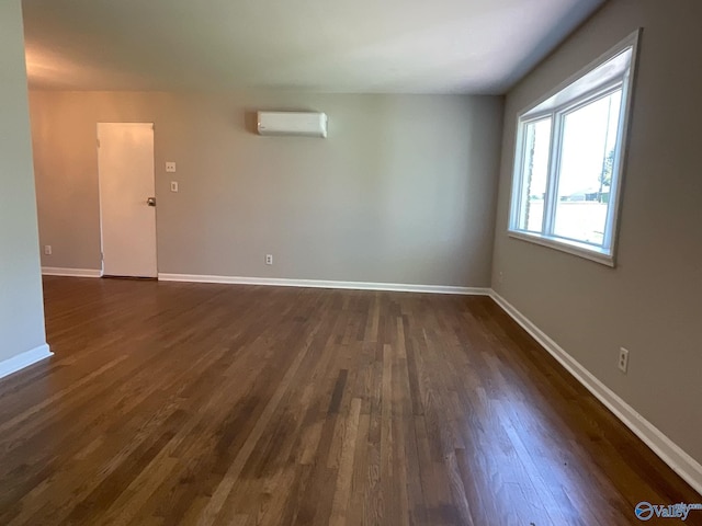 spare room with dark wood-type flooring, baseboards, and a wall unit AC