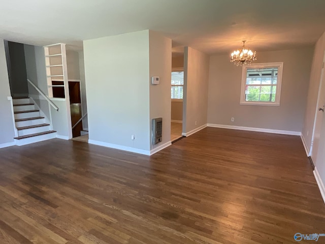 empty room featuring a notable chandelier, baseboards, heating unit, stairs, and dark wood-type flooring