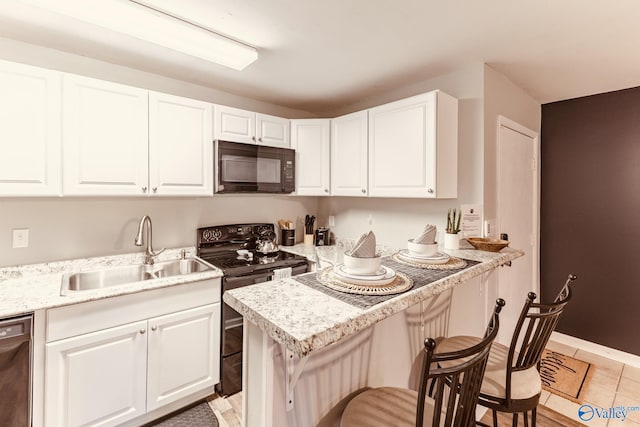 kitchen featuring a breakfast bar, white cabinetry, a sink, and black appliances