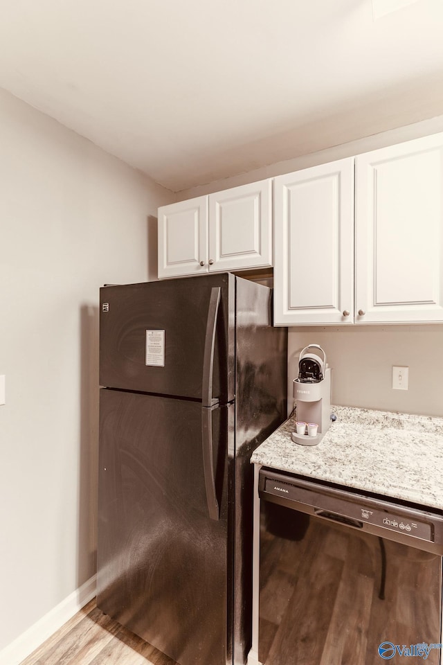 kitchen with baseboards, white cabinets, light wood-type flooring, light stone countertops, and black appliances