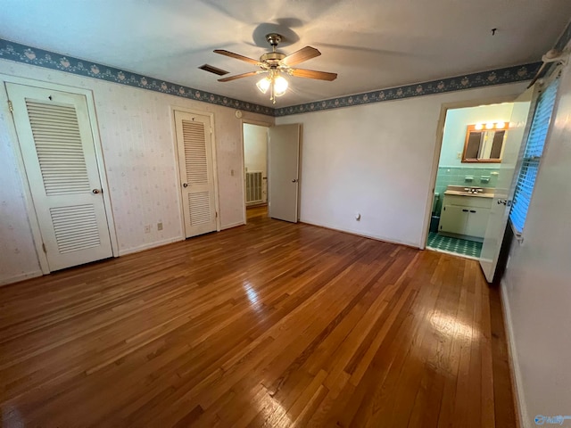 unfurnished bedroom featuring multiple closets, ensuite bath, tile patterned flooring, and ceiling fan