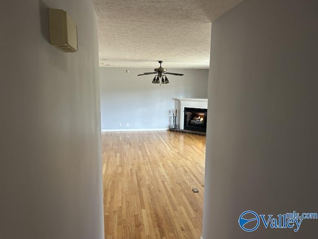 unfurnished living room featuring a textured ceiling, a brick fireplace, ceiling fan, and light hardwood / wood-style flooring