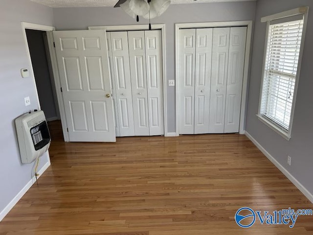 unfurnished bedroom with heating unit, ceiling fan, wood-type flooring, and multiple closets