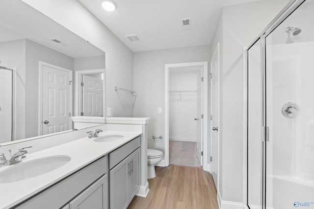 bathroom featuring wood-type flooring, toilet, a shower with shower door, and vanity