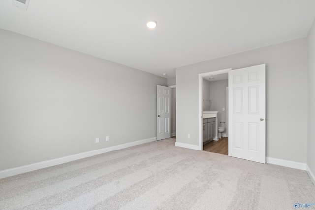 unfurnished bedroom featuring light colored carpet and ensuite bathroom