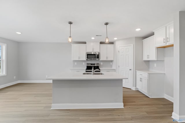 kitchen with hanging light fixtures, stainless steel appliances, an island with sink, and white cabinets