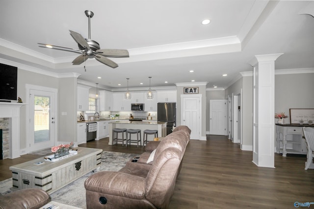 living room with dark hardwood / wood-style floors, ornamental molding, decorative columns, a fireplace, and ceiling fan